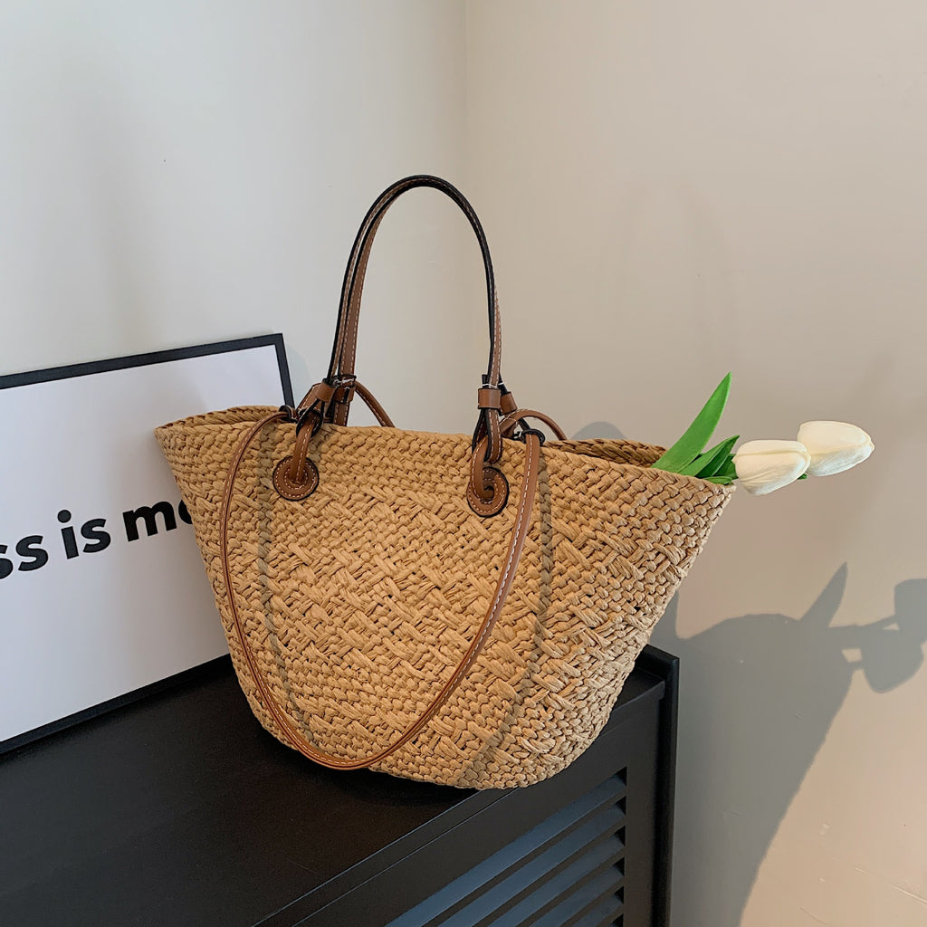 The Greemnest Artisan Paper Rope Woven Bag with drawstring closure and dark brown handles sits on a black cabinet. Two white tulips peek from the eco-friendly bag, with a framed sign partially visible nearby against a light wall.